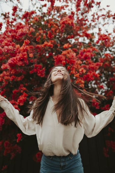 Mujer con cabello largo, cabeza arriba con ojos cerrado abriendo los brazos