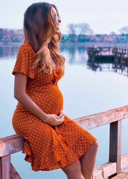 Mujer sentada en un muelle tocándose la panza de embarazada