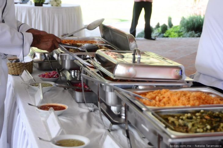 Barra de un buffet mostrando los platillos mientras una persona los toma con una cuchara 