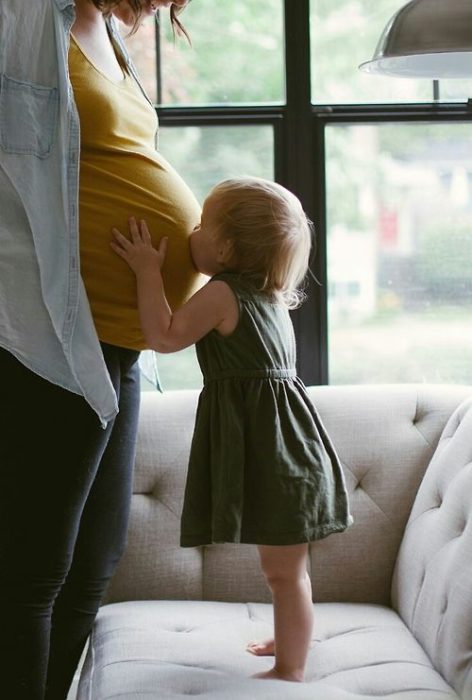 Bebé besando a su mamá embarazada en la panza