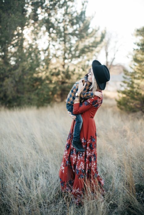 Cosas graciosas que dicen los niños; mujer rubia, vestido rojo y largo de flores, con sombrero negro; mamá cargando a su hijo en el campo