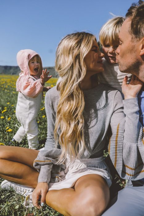 Cosas graciosas que dicen los niños; familia sentada en el campo con flores; mujer rubia de cabello largo y ondulado; mamá, papá y dos hijos