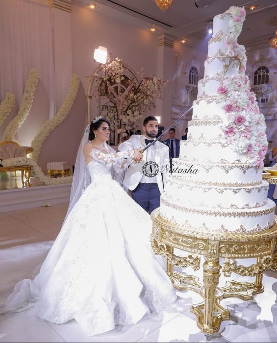 Pareja de novios sosteniendo un cuchillo para cortar su primera rebanada de un pastel gigante