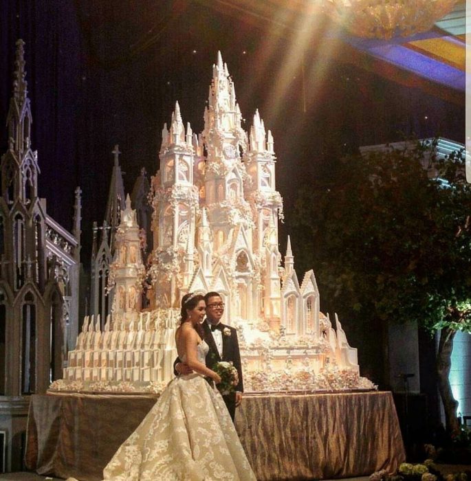 Pareja de novios parados frente a un pastel de bodas impresionante en forma de castillo 