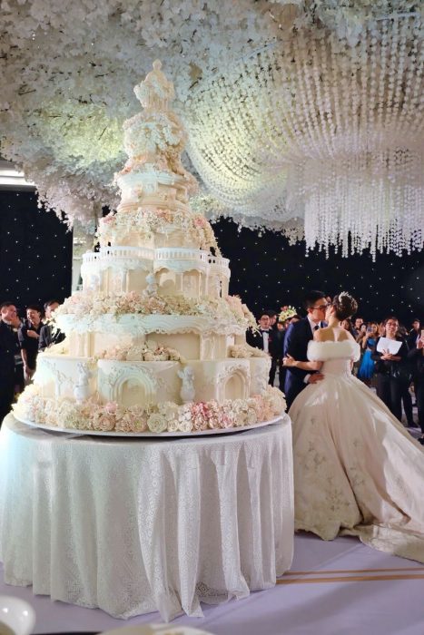 Pareja de novios parados frente a un enorme pastel de bodas 