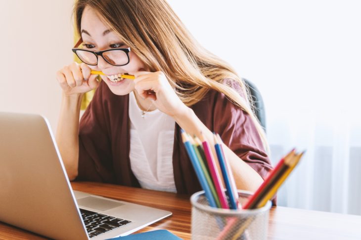 Mujer mordiendo lapiz frente a computadora