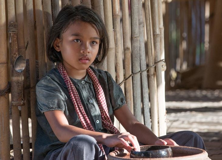 Sareum Srey Moch sentada en el piso recargada en una pared de bambú, escena de la película Se lo llevaron: Recuerdos de una niña de Camboya