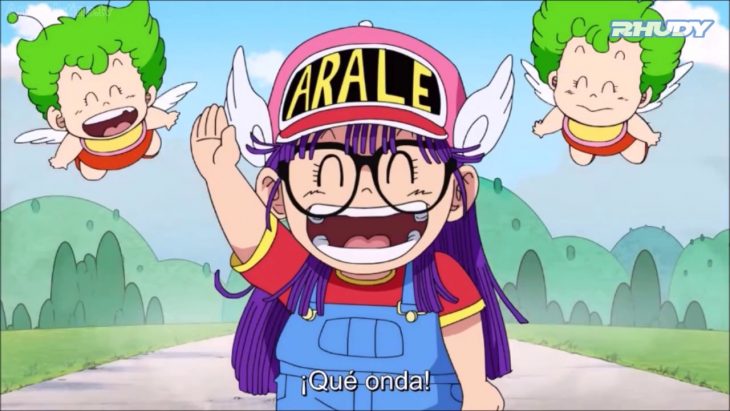 Arale usando su clásico overol y gorra rosa, saludando 