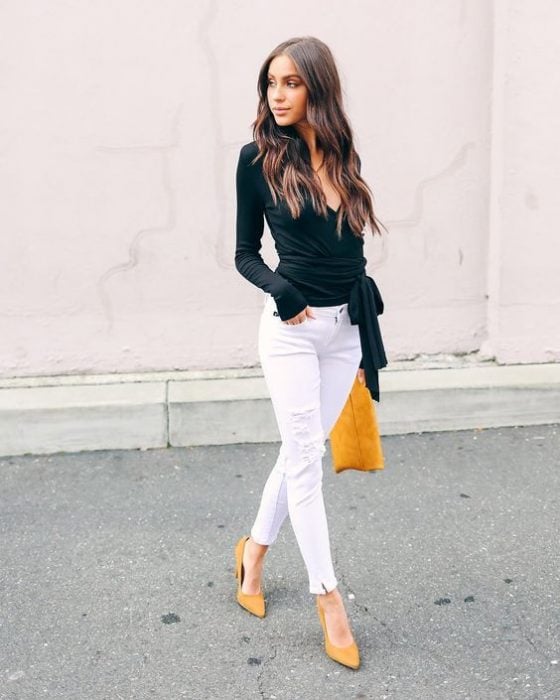 Mujer joven vistiendo pantalón blanco y blusa negra con bolsa amarilla