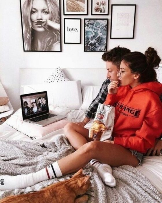 Pareja de novios abrazados, comiendo papas fritas y viendo una película sobre la cama