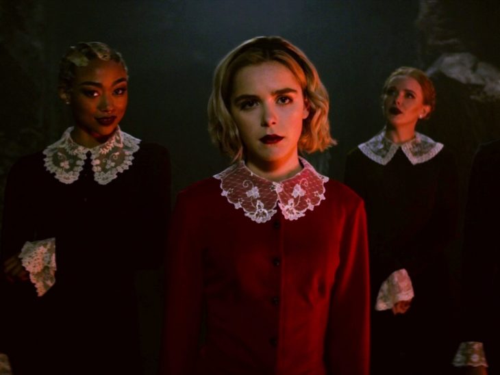 Escena de la serie Sabrina; Actriz que interpreta a Sabrina parada junto a dos de sus rivales mientras usan las batas de su escuela 