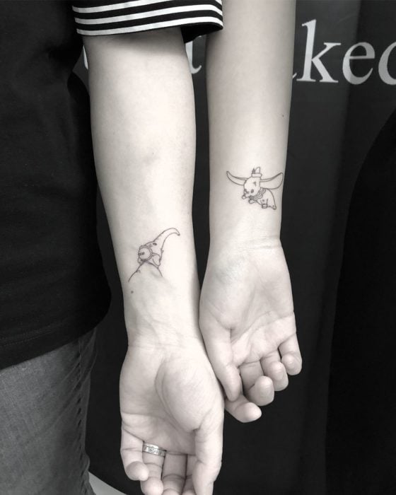 Tatuaje minimalista de Dumbo volando y su mamá para parejas o amigas en el antebrazo