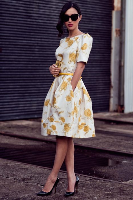 Ideas de vestidos para boda en jardín al aire libre; mujer con vestido blanco, con flores amarillas, cinto amarillo delgado y tacones stiletto