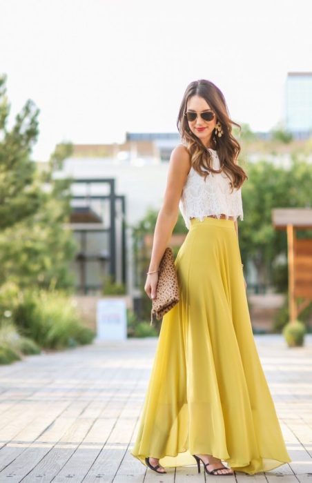 Ideas de vestidos para boda en jardín al aire libre; chica con falda larga y amarilla, top blanco con encaje, sandalias de tacón y bolsa de mano de animal print