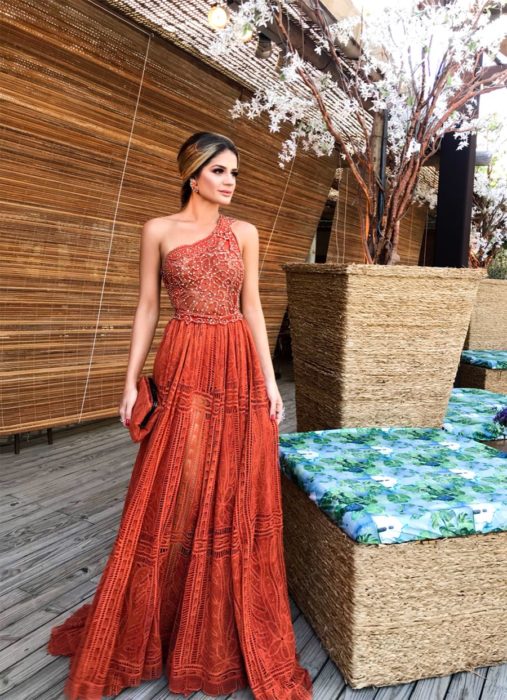 Ideas de vestidos para boda en jardín al aire libre; mujer con vestido largo de un solo hombro, color terracota, con encaje