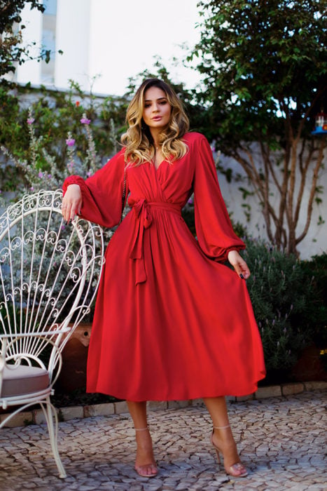 Ideas de vestidos para boda en jardín al aire libre; mujer con vestido rojo de escote cruzado, con listón en la cintura y mangas