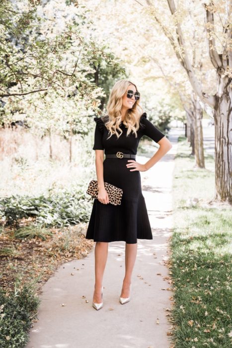 Chica parada en medio de la calle usando un vestido negro con un cinto, tacones dorados y cartera animal print 