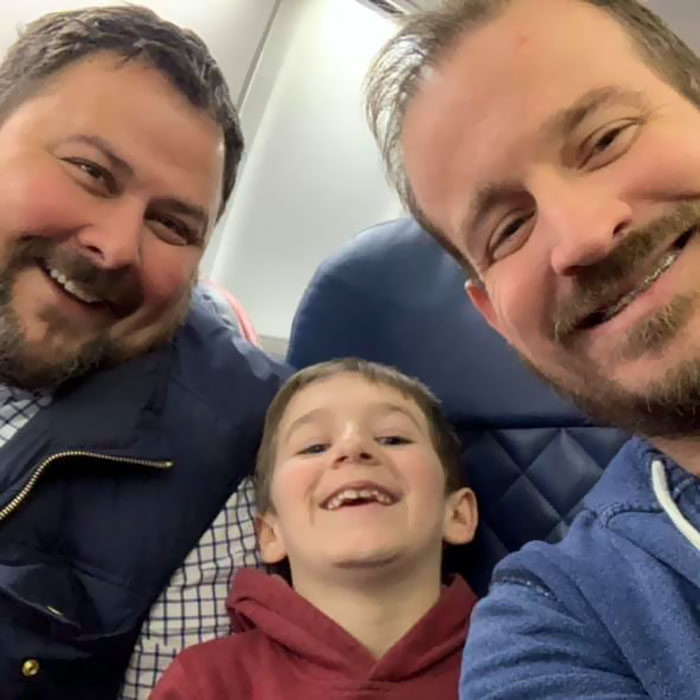 paul y gregg padres que adoptaron a un niño, posando con el pequeño durante un viaje en avión 