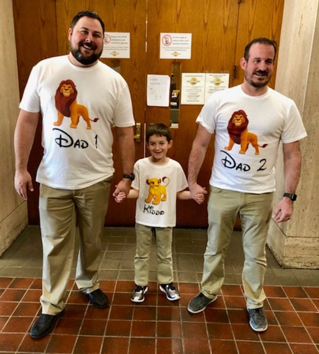 Paul y Gregg pareja que adoptó a un niño, celebrando la adopción con camisas del rey león que dicen papá-hijo-papá