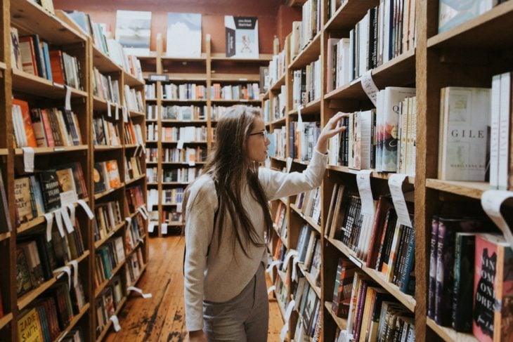 Chica dentro de un pasillo de biblioteca buscando un libro
