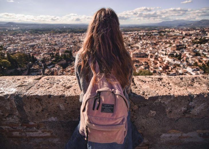 chica de espaldas mostrando su mochila de color rosa y admirando en paisaje cubierto de casas y edificios antiguos 