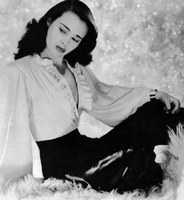 Gloria Vanderbilt posa en su juventud con una blusa blanca de olanes abierta y una falda negra