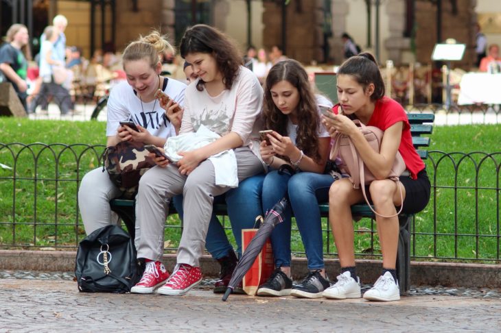 cuatro jovencitas viendo sus celulares sentadas en un jardín