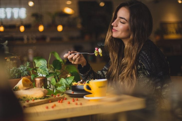 mujer cabello largo sentada en la mesa comiendo ensalada