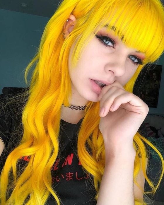 Chica con cabello largo, ondulado, con fleco y de color amarillo brillante