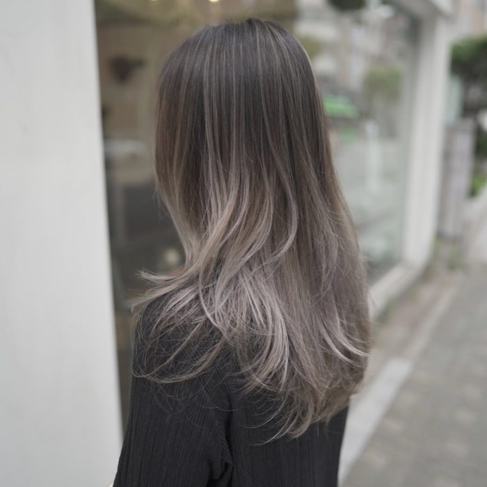 Chica posando de lado, con el rostro cubierto por su cabello color rubio champiñón 