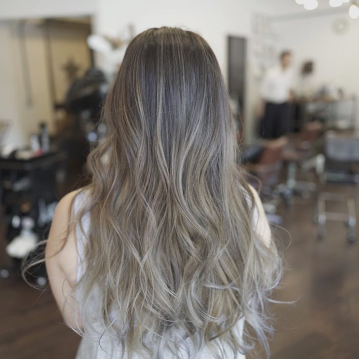 Mujer de espaldas mostrando su cabellera larga con cabello color rubio champiñón 