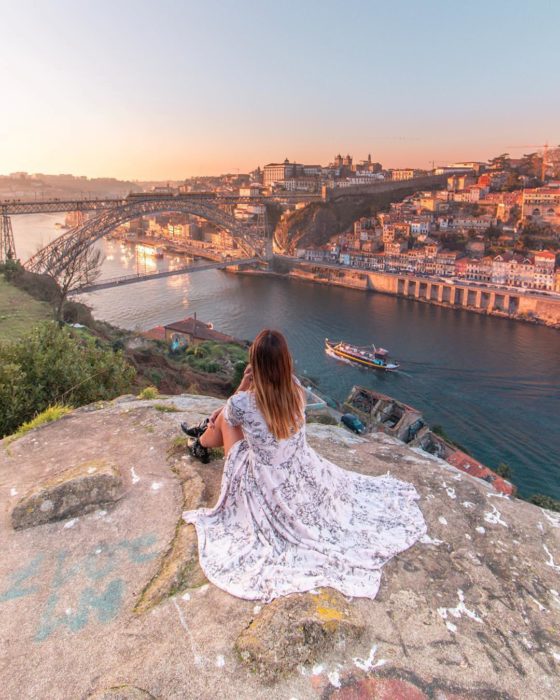 Cosas que debes hacer en vez de enamorarte; chica de vestido largo sentada en una montaña viendo la ciudad y el río