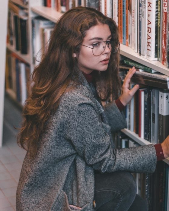 Cosas que debes hacer en vez de enamorarte; chica rubia con lentes de aumento en una biblioteca viendo libros