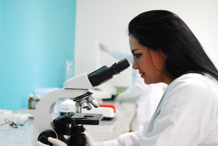 Mujer de cabello negro ve a través de un microscopio