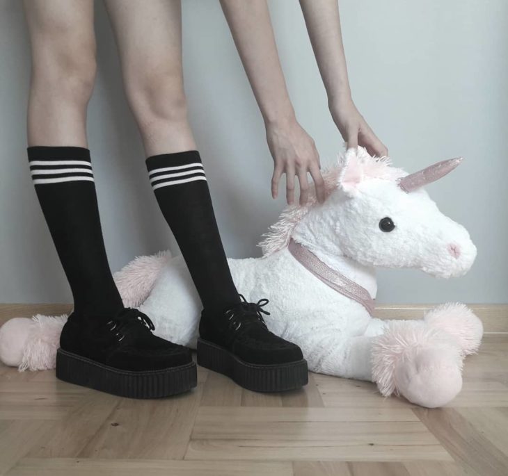 Mujer usando creepers, zapatos con suelas altas y agarrando un peluche de unicornio 