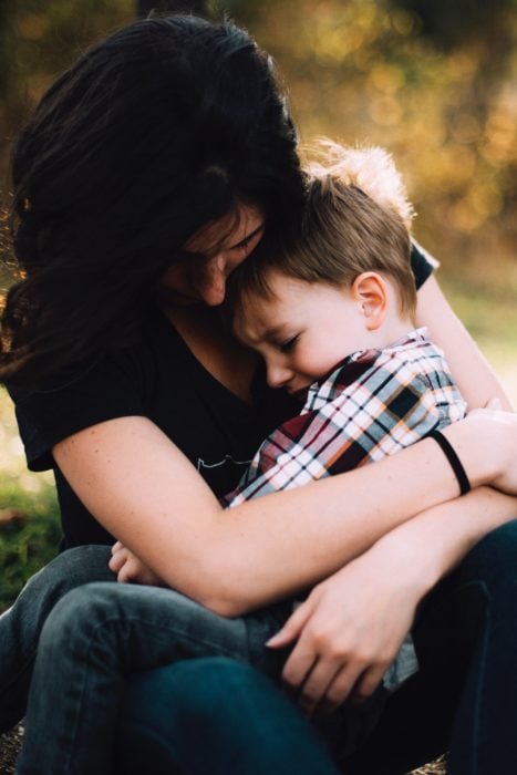 Una mamá sentada abraza en su regazo a su hijo con camisa de cuadros