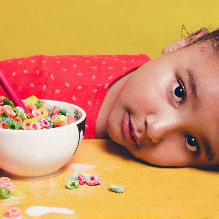 Una niña está recostada sobre la mesa en donde se observa un plato con cereal de colores