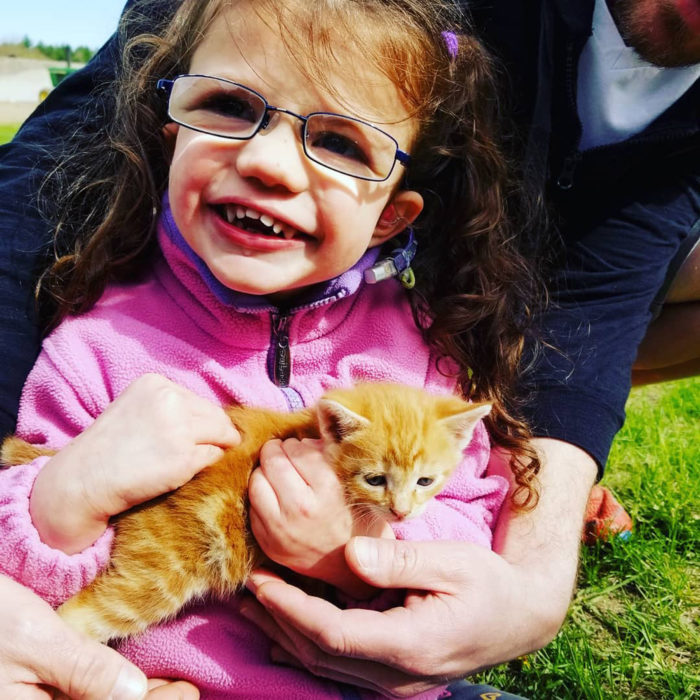 Morey Belanger con un pequeño gato en sus brazos y una persona abrazándola