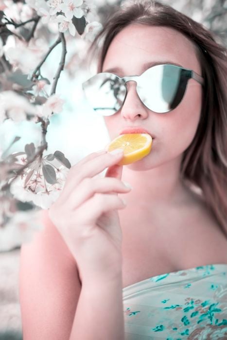 Chica con lentes espejo comiendo limón