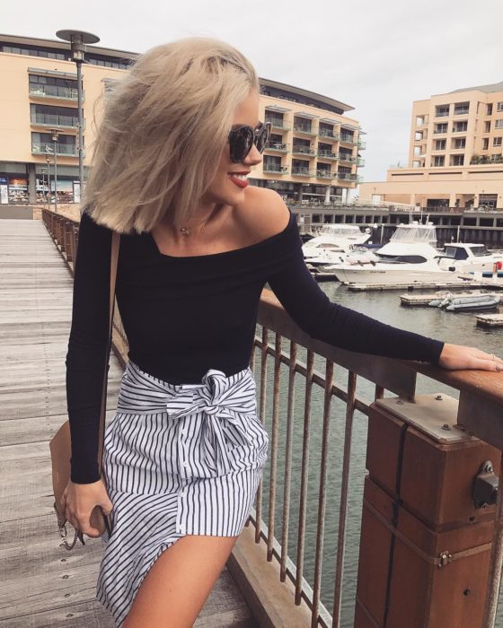 Faldas para el verano; chica rubia en el muelle con blusa sin hombros y falda rayada