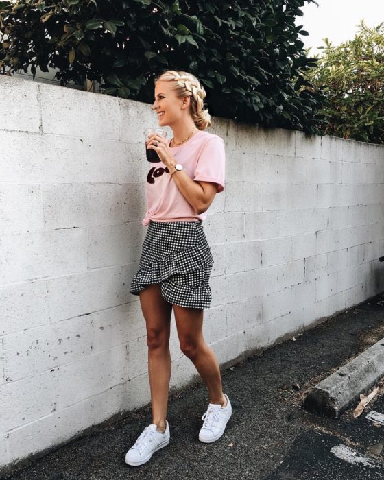 Faldas para el verano; mujer tomando bebida, con peinado de trenza y chongo, con blusa básica rosa y falta de cuadros cruzada