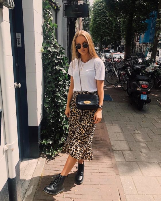 Faldas para el verano; chica rubia con lentes de sol, blusa blanca básica, falda larga de animal print y botas militares Dr. Martens