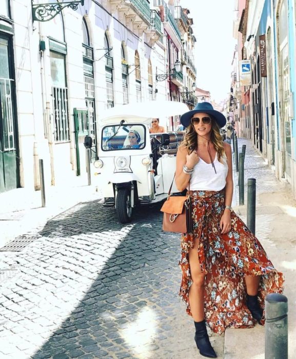 Faldas para el verano; chica en calle empedrada, con sombrero, lentes de sol, blusa de tirantes blanca básica y falda floreada con abertura