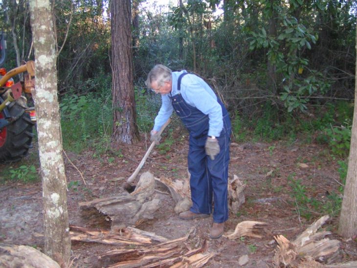 Kenneth Smith, hombre mayor cortando leña con un overol de mezclilla 