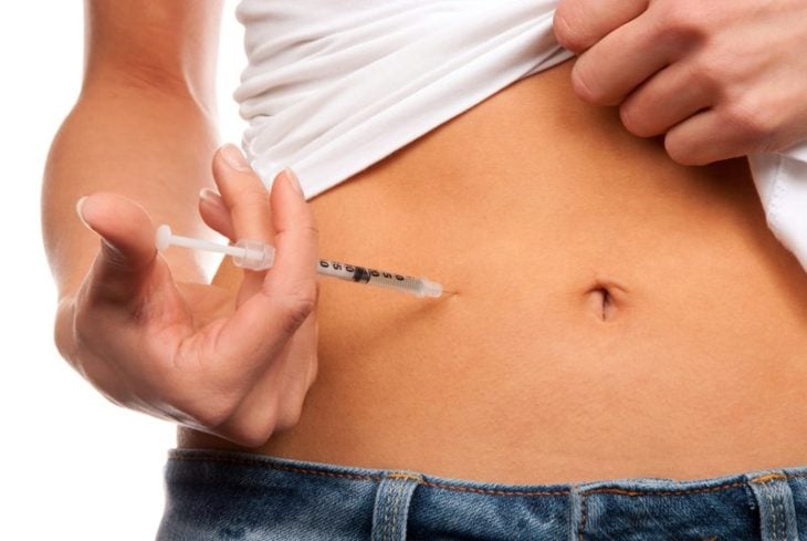 una mujer se inyecta insulina en su abdomen mientras levanta su blusa blanca