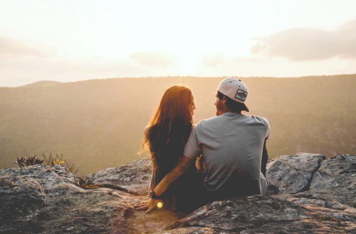 pareja joven sentados en lo alto de una montaña