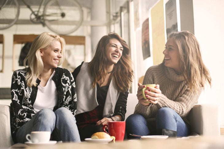 tres mujeres hablan en un café, una sostiene una taza