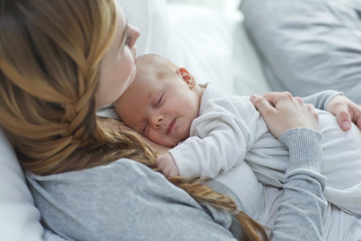 una mamá con su bebé en brazos durmiendo y sonríe