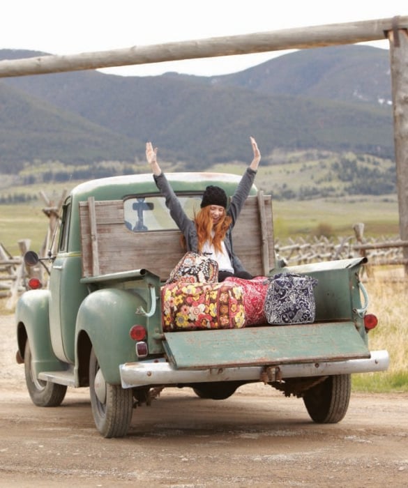 Chica en la parte trasera de una camioneta con maletas yendo de viaje