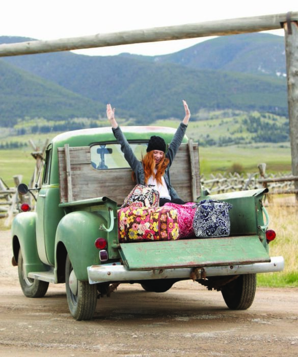 Chica en la parte trasera de una camioneta con maletas yendo de viaje